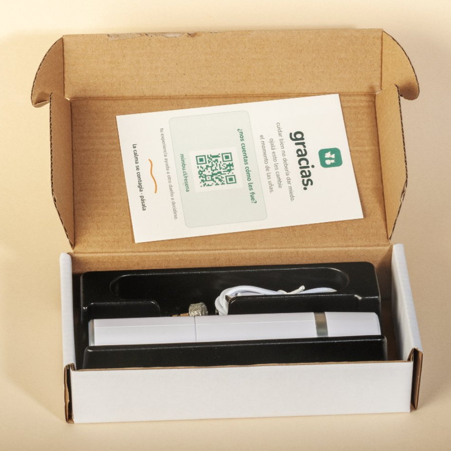 la caja abierta: en la tapa, la tarjeta que dice «gracias. cuidar bien no debería dar miedo. ojalá esto les cambie el momento de las uñas»; en la bandeja, la lima, el cable USB-C y el cabezal de repuesto